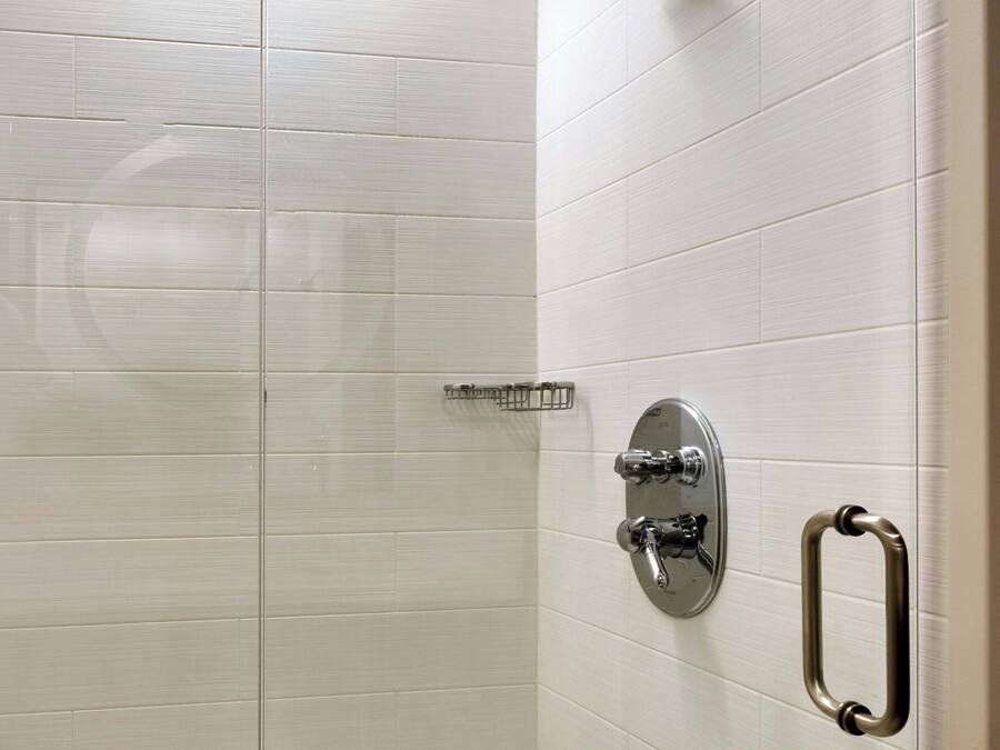 A shower with a glass door, a handheld showerhead, and a wall-mounted faucet.