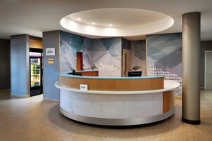 A reception desk with a modern design, a refrigerator stocked with beverages, and a large abstract mural on the wall.