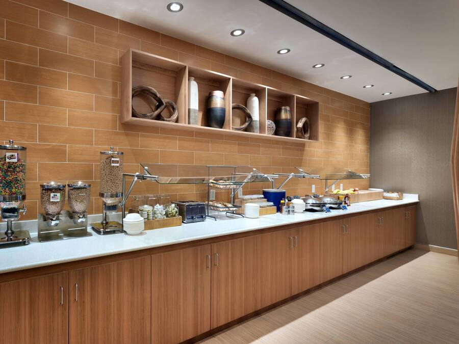 A modern kitchen with a long counter, various food dispensers, and a wooden cabinet.