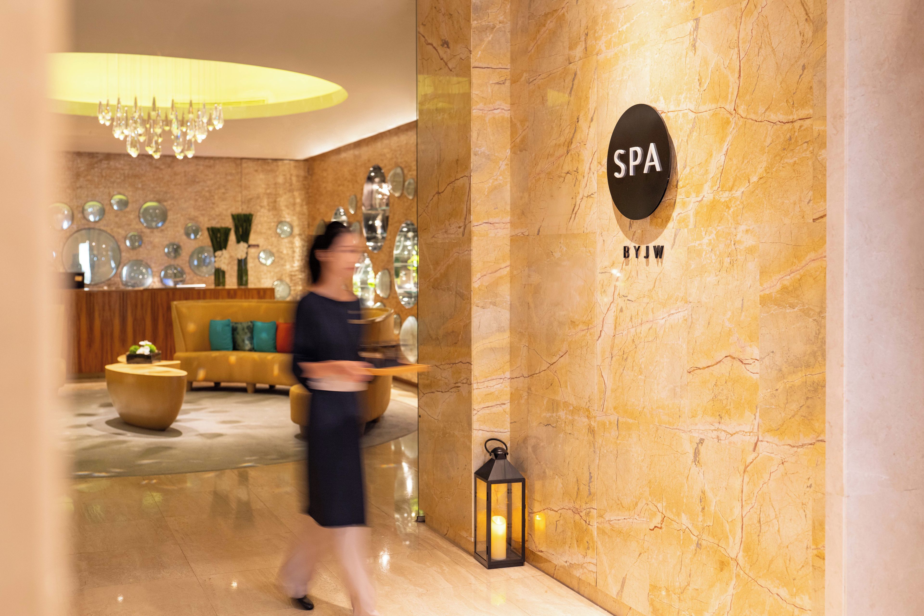 A spa area with a marble wall, a sign reading "SPA BYJW", and a modern chandelier.