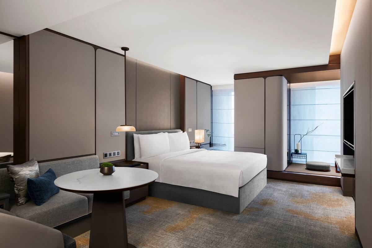 Ein modernes Hotelzimmer mit einem großen Bett, einer Couch, einem kleinen Tisch und einem Fernseher.