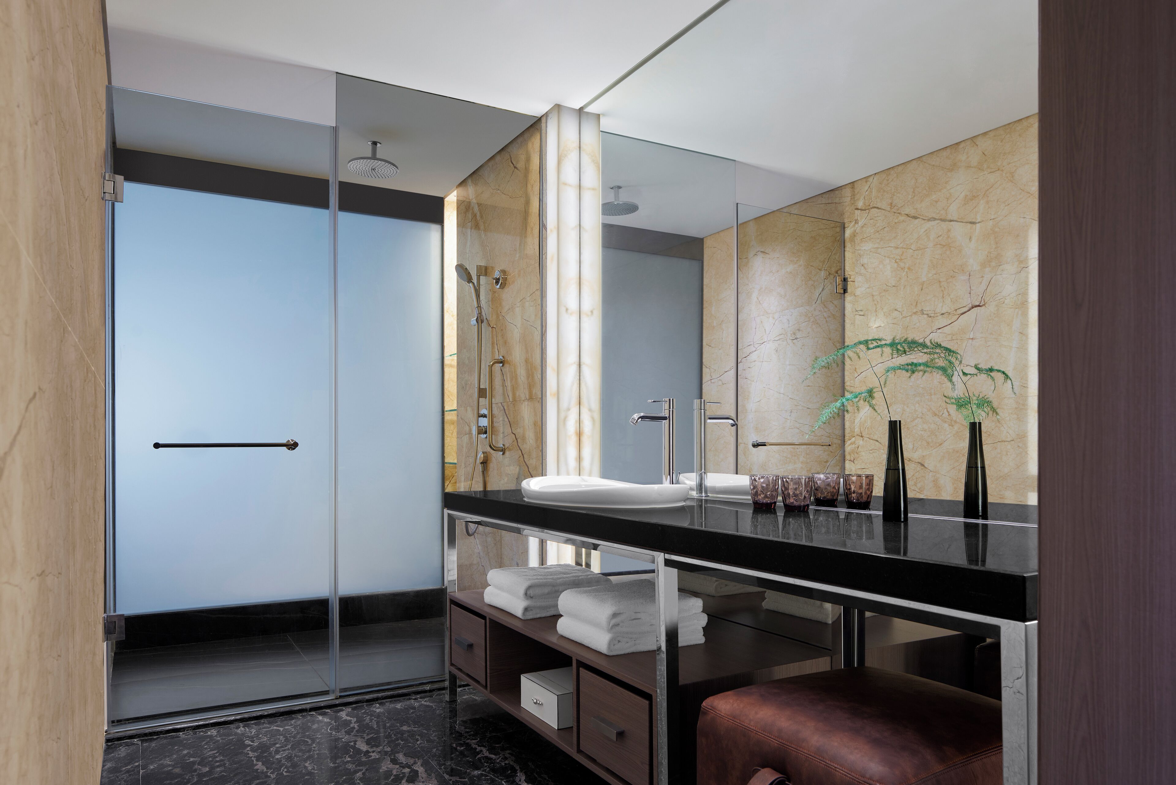 A modern bathroom with a glass shower enclosure, a black countertop, a white sink, and a large mirror.