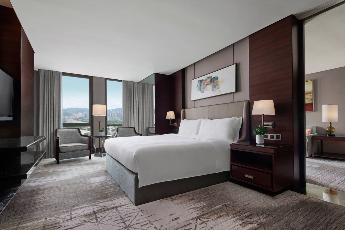 Ein modernes Hotelzimmer mit einem großen Bett, einem Schreibtisch, einem Stuhl und Blick auf die Stadt.