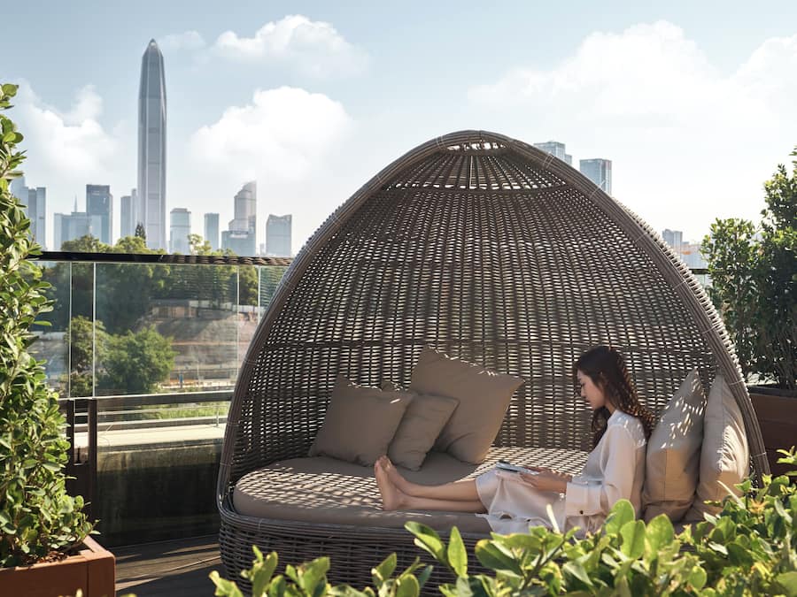 A wicker egg chair with cushions on a rooftop terrace with a city skyline in the background.