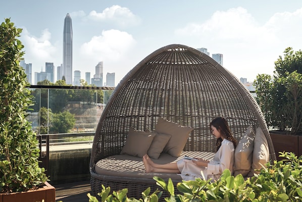 A wicker egg chair with cushions on a rooftop terrace with a city skyline in the background. - JW Marriott Hotel Shenzhen (Shenzhen)