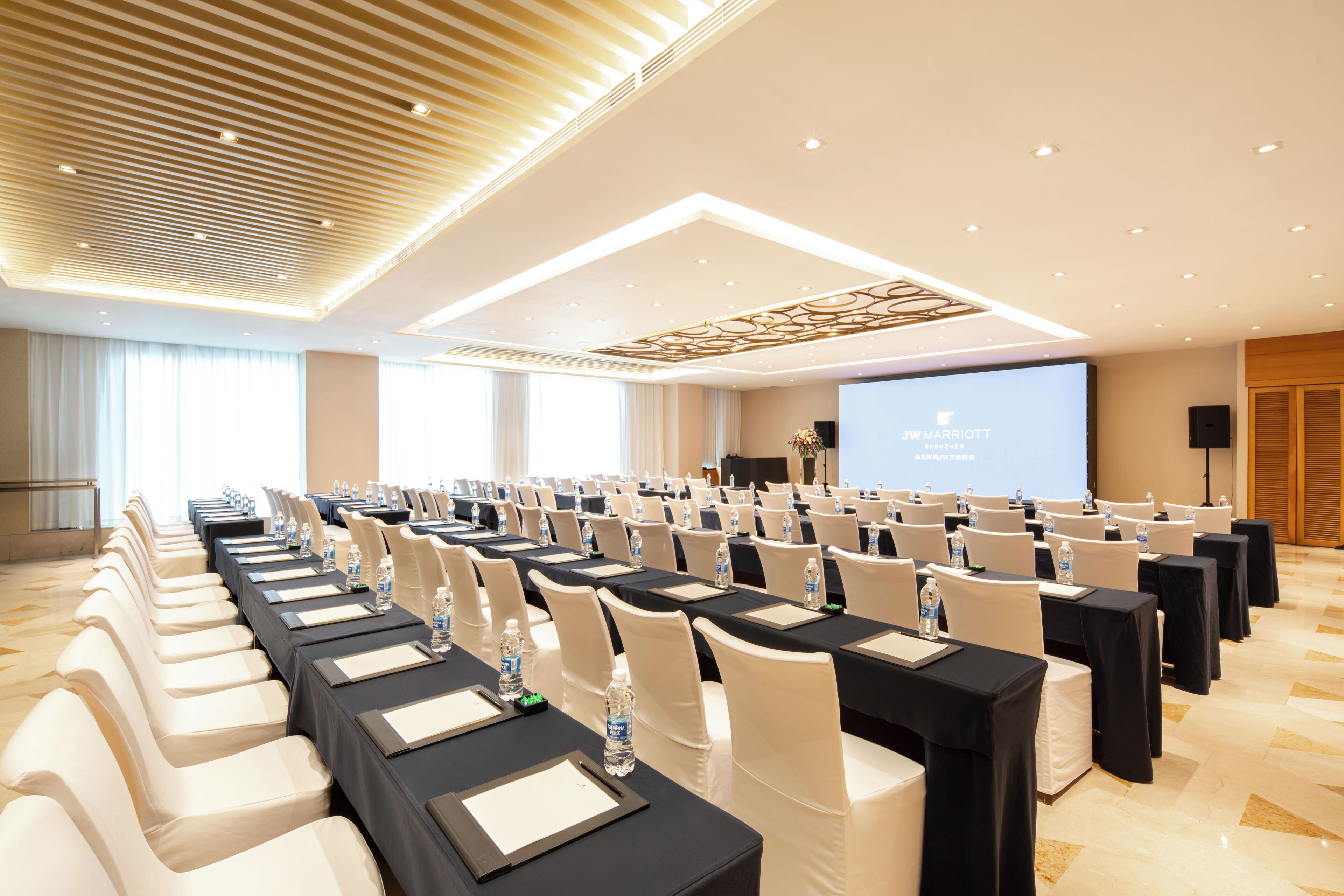 A conference room with rows of tables and chairs, a projector screen, and a stage.