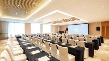 A conference room with rows of tables and chairs, a projector screen, and a stage.