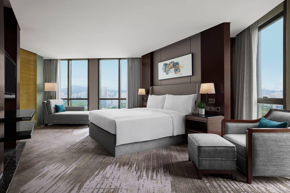 Ein modernes Hotelzimmer mit einem großen Bett, zwei Sesseln, einem Schreibtisch und Blick auf die Stadt.