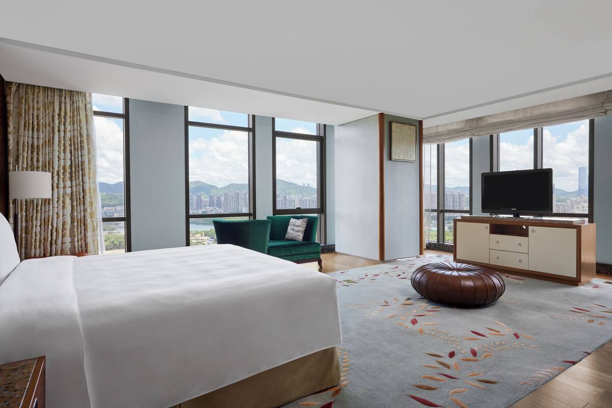 Ein modernes Hotelzimmer mit einem großen Bett, einem Fernseher, einem grünen Sessel und Blick auf die Stadt.