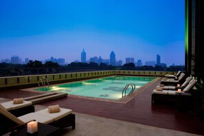 Una piscina en la azotea con sillones de descanso y vistas al horizonte de la ciudad.