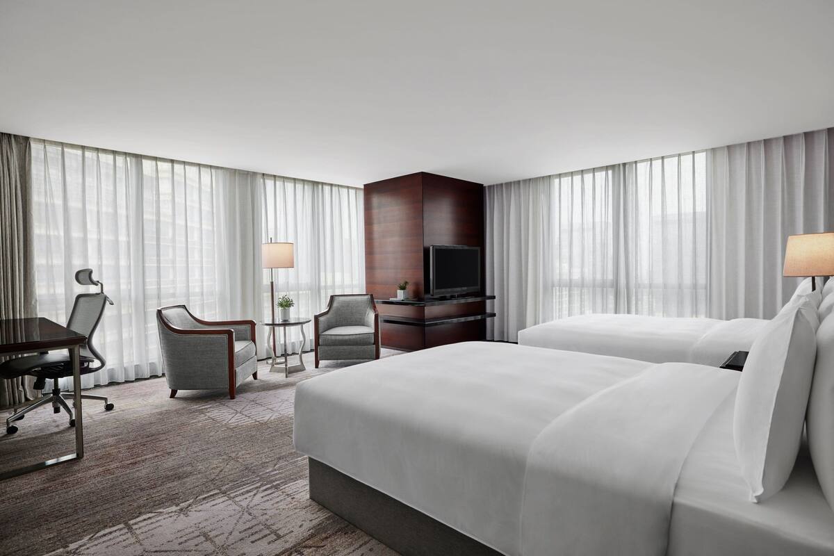 A hotel room with a large bed, a desk with a chair, a TV, and a small table with a lamp.