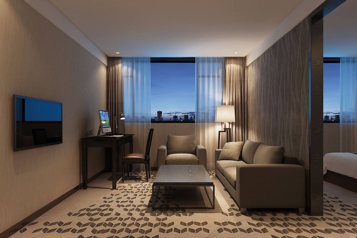 A modern hotel room with a city view, a flat-screen TV, a desk with a laptop, a sofa, and a bed.