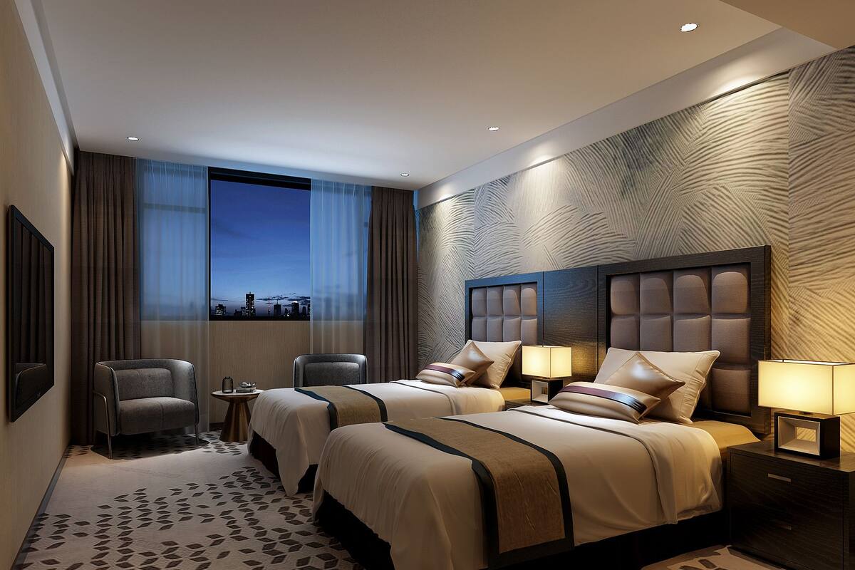 A hotel room with two beds, a chair, a nightstand, and a view of the cityscape.