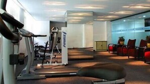 A gym with exercise equipment, a treadmill, and a seating area with chairs and a small table. - Henry Business Hotel (Guangzhou)