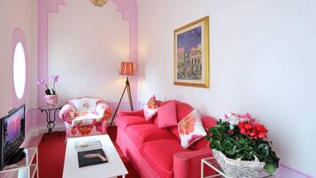 A pink-themed living room with a sofa, armchair, and a TV on a stand.
