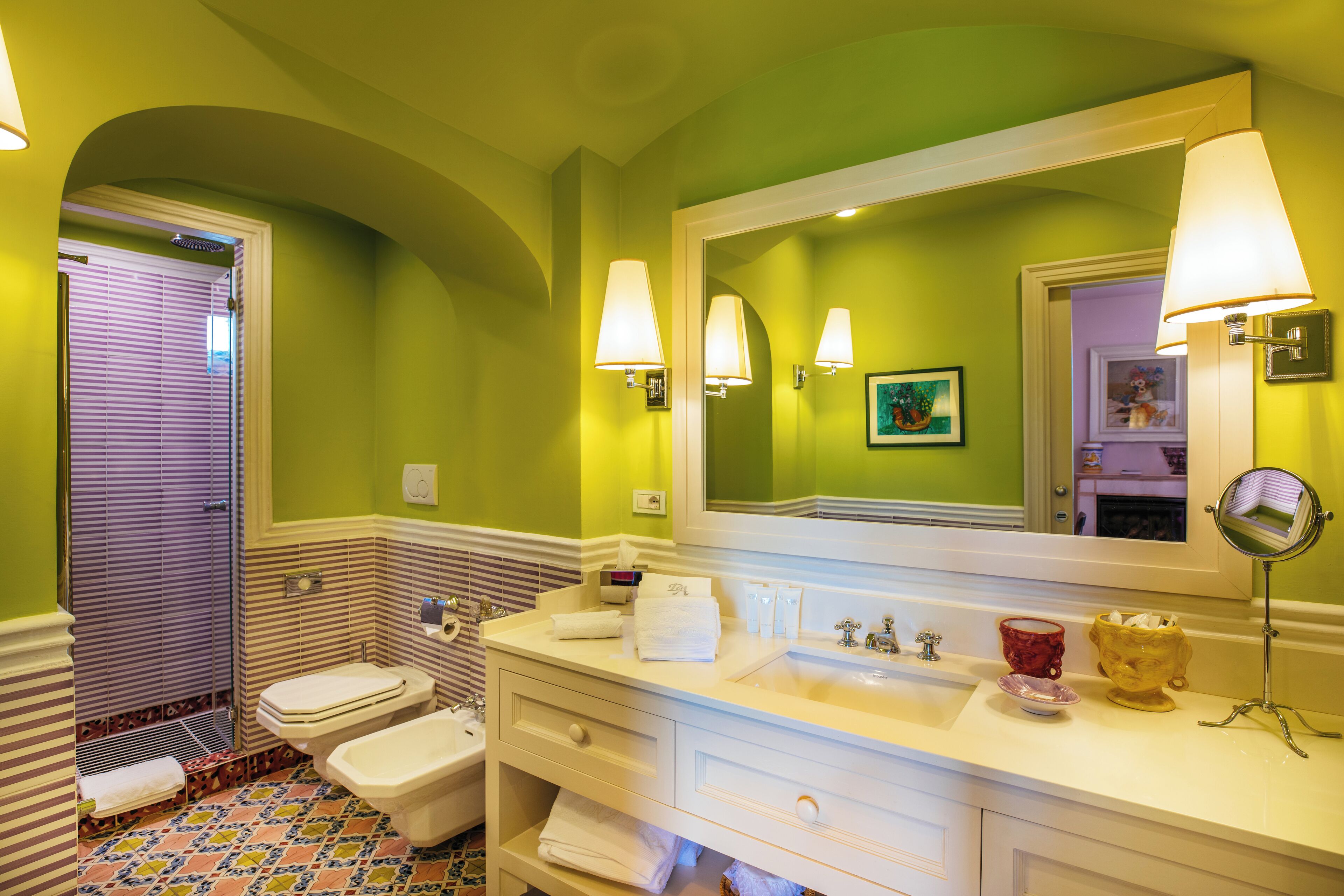 A bathroom with a large mirror, two toilets, a sink, and a vanity with drawers.