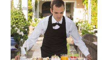 A waiter serving breakfast outdoors with a table set with plates, glasses, and a jug.