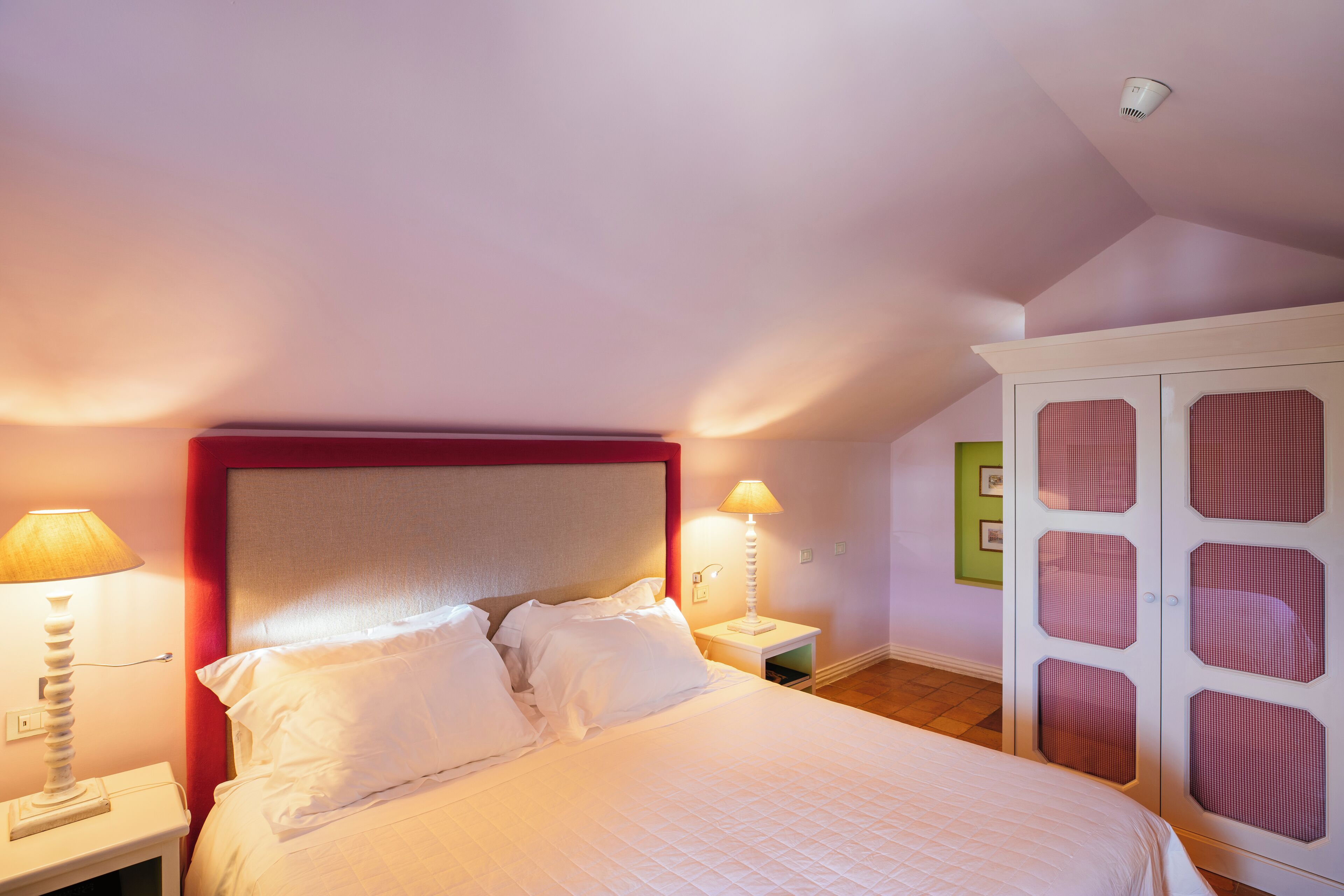 Un dormitorio con cama, mesitas de noche, armario y lámparas de pared.