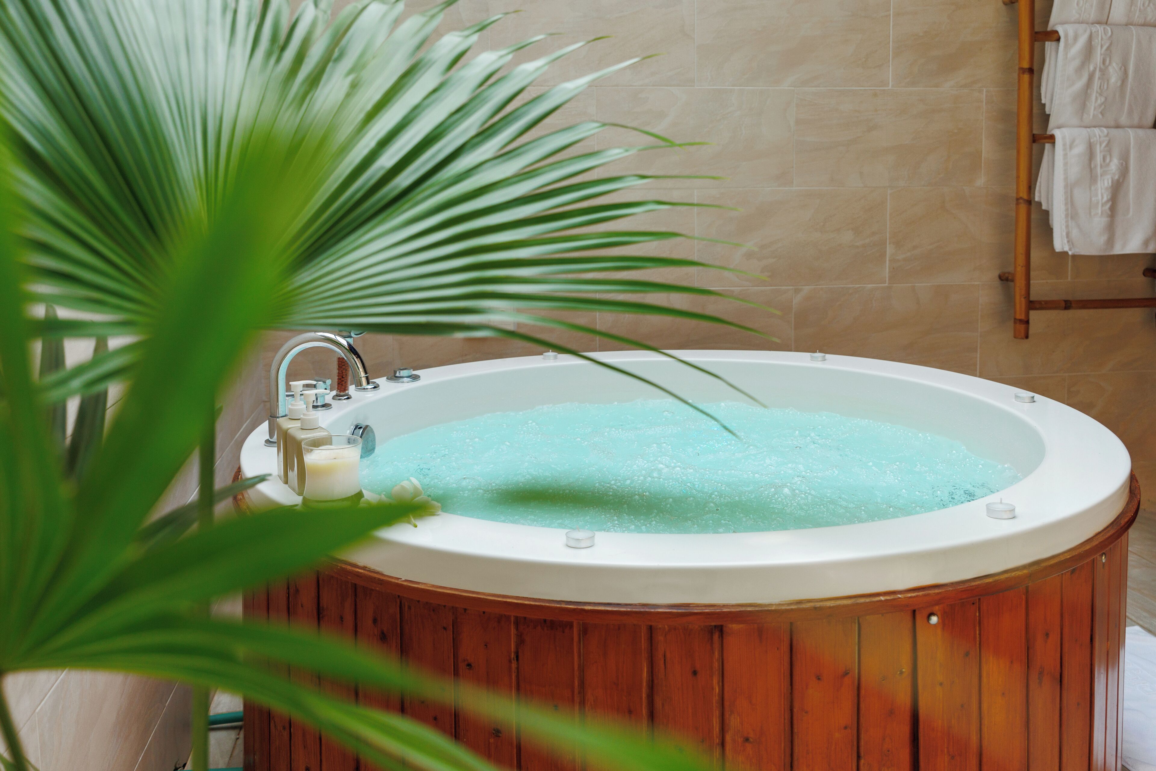 Una bañera de madera llena de agua, un grifo y una botella de jabón.