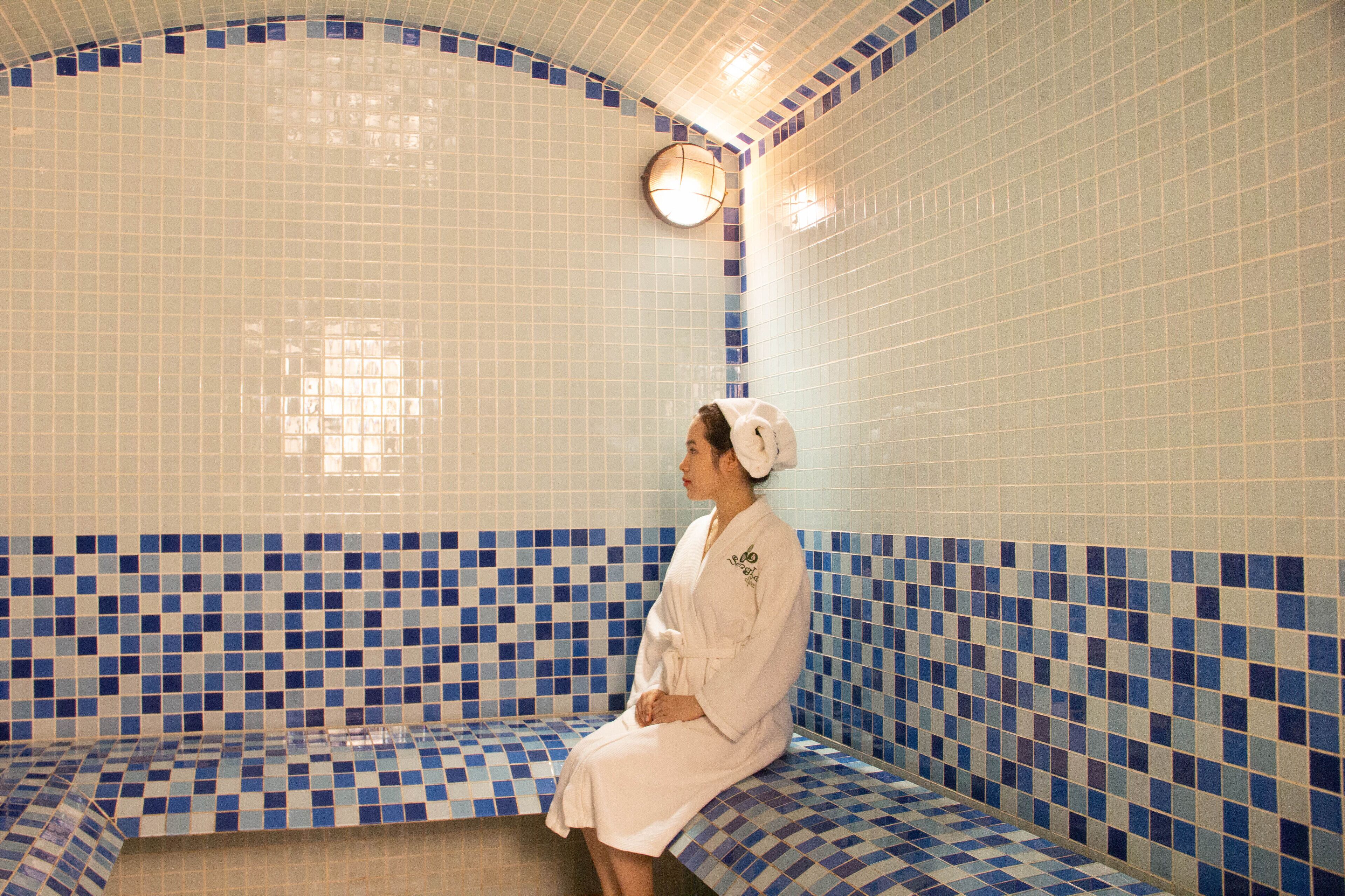 A person sitting on a bench in a tiled room with a checkered pattern on the floor and walls.