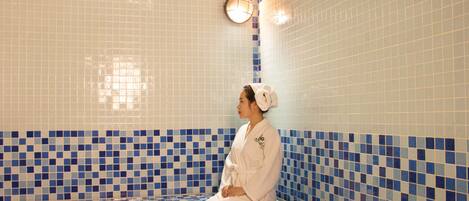 A person sitting on a bench in a tiled room with a checkered pattern on the floor and walls.