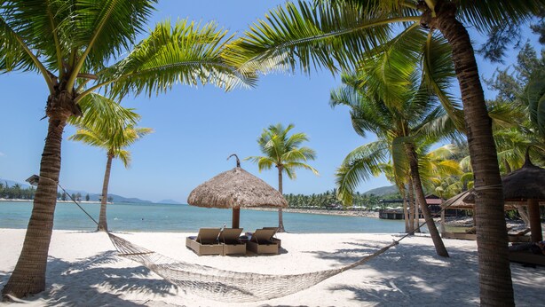 A beach with a hammock, lounge chairs, and a thatched umbrella. - Diamond Bay Resort and Spa (Nam Nha Trang)