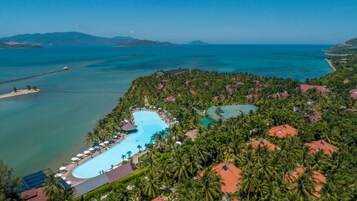 Vista aérea de un resort con una gran piscina, palmeras y vistas al océano.