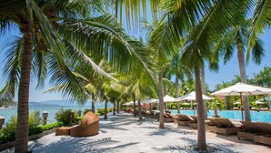 A resort pool area with lounge chairs, umbrellas, and palm trees. - Diamond Bay Resort and Spa (Nam Nha Trang)