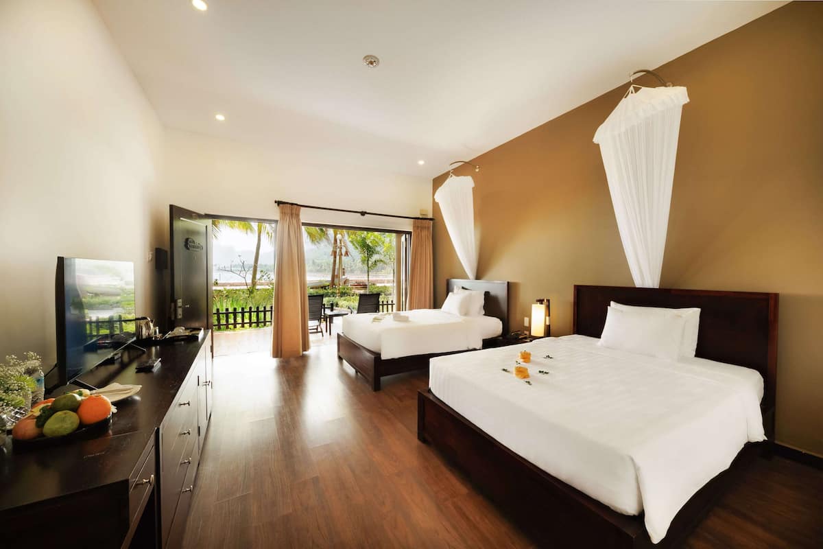A hotel room with two beds, a TV, a desk with a computer, and a view of the outdoors.