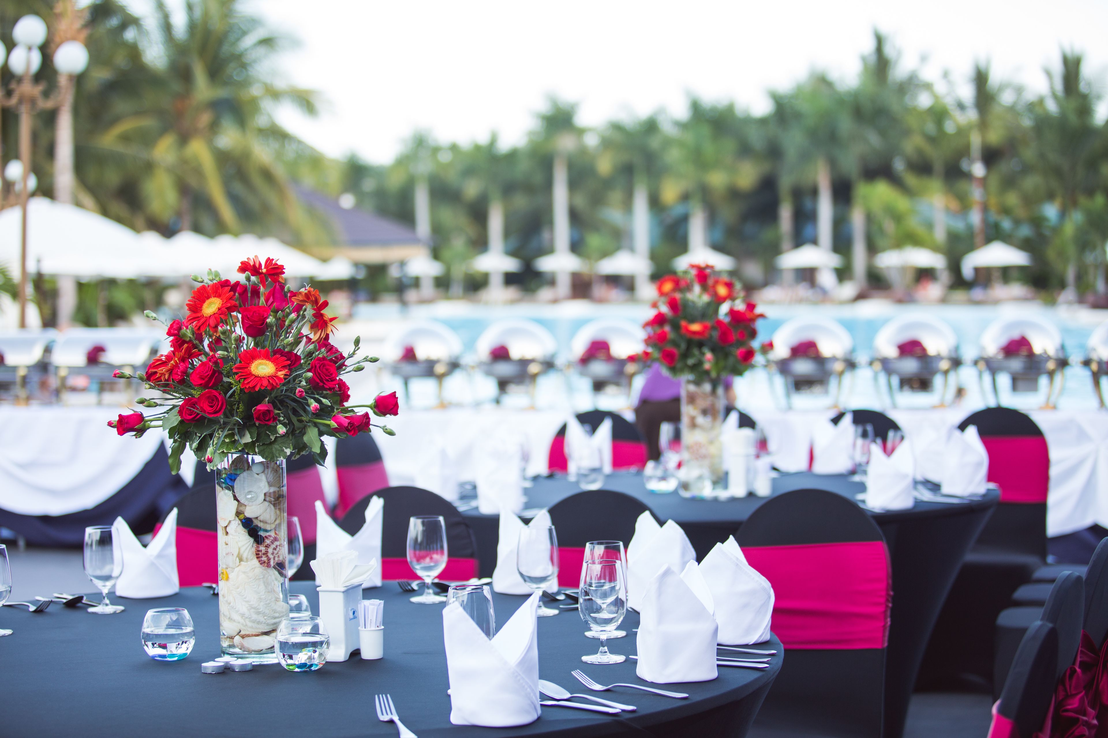 A dining area with tables set for a formal event, featuring clear glassware, folded napkins, and floral centerpieces.