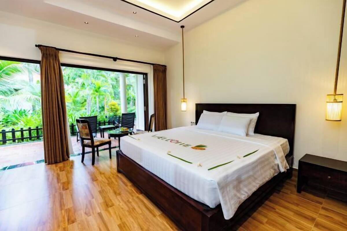 A hotel room with a large bed, a desk, and a view of greenery.