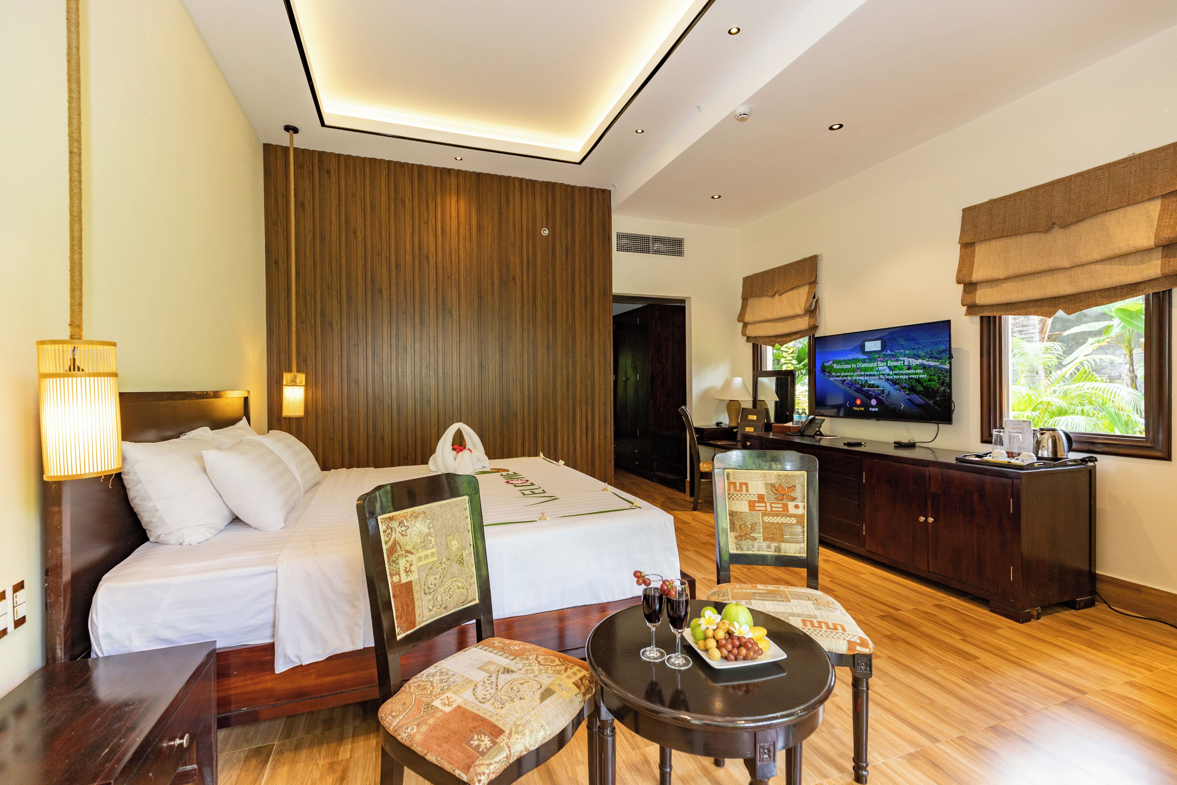A hotel room with a bed, a desk, a television, and a dining table with fruit.