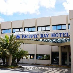 The Pacific Bay Hotel with a covered entrance and palm trees in the foreground. - Pacific Bay Hotel (Tamuning)