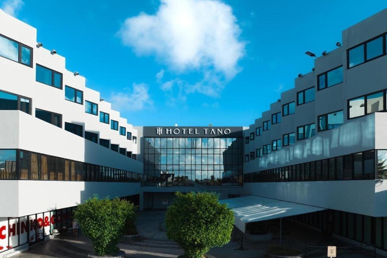 Un hotel moderno con fachada de vidrio central y un letrero que dice "HOTEL TANO".