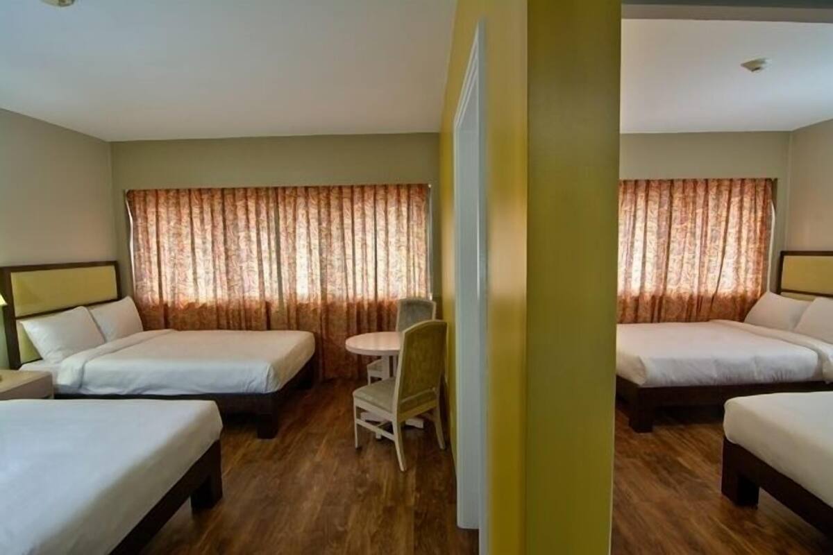 A hotel room with two single beds, a small round table with a chair, and a window with curtains.