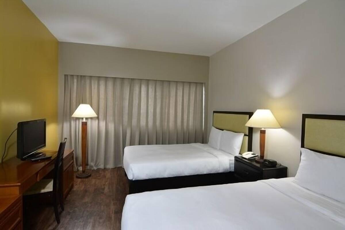 A hotel room with two beds, a desk with a computer, and two bedside lamps.