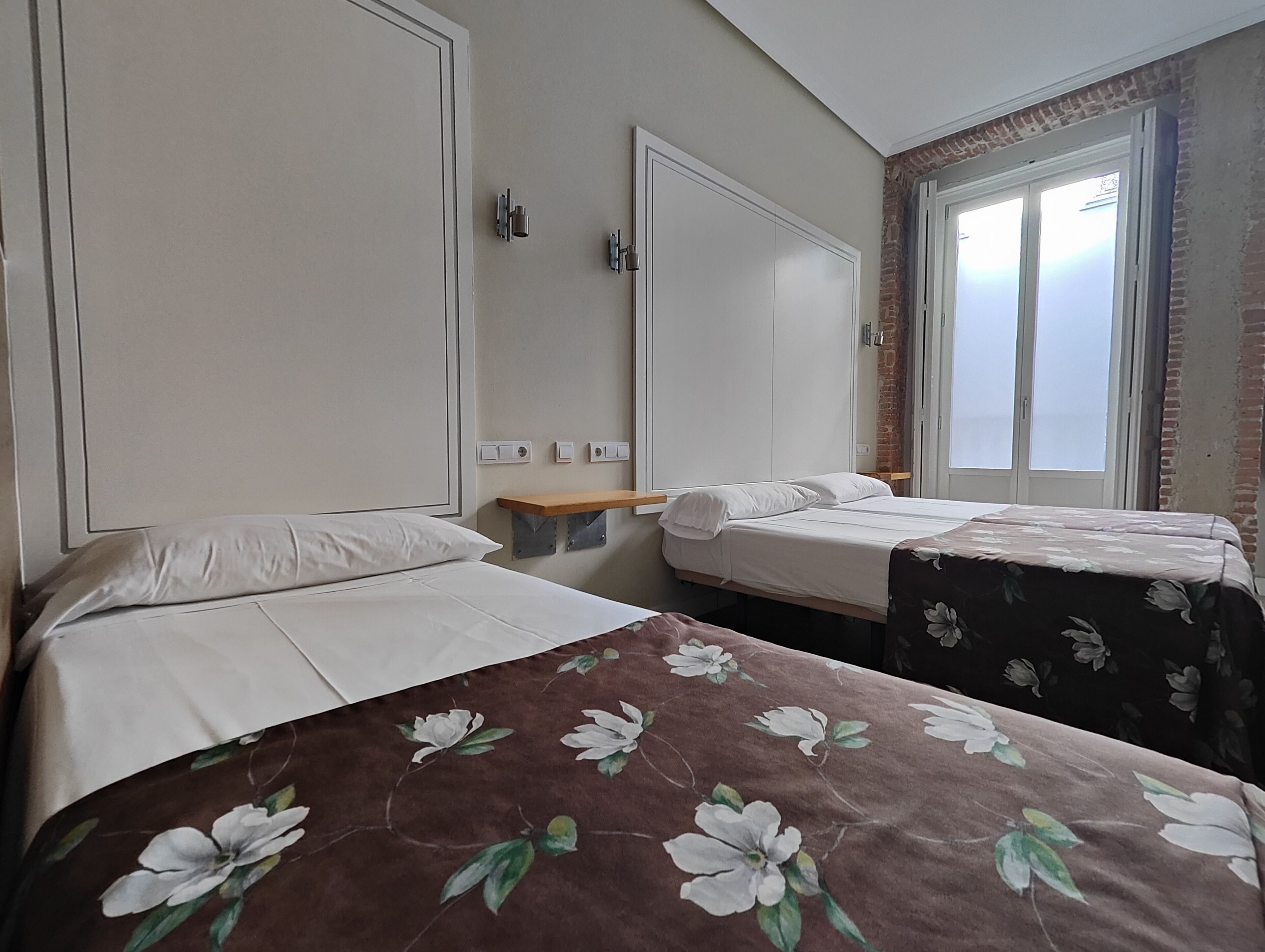 A hotel room with two beds, a wooden shelf, and a window with a view.