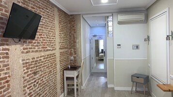 Ein Flur mit Backsteinwand, einem Wand-Fernseher, einem kleinen Schreibtisch und einer Tür zu einem anderen Raum.