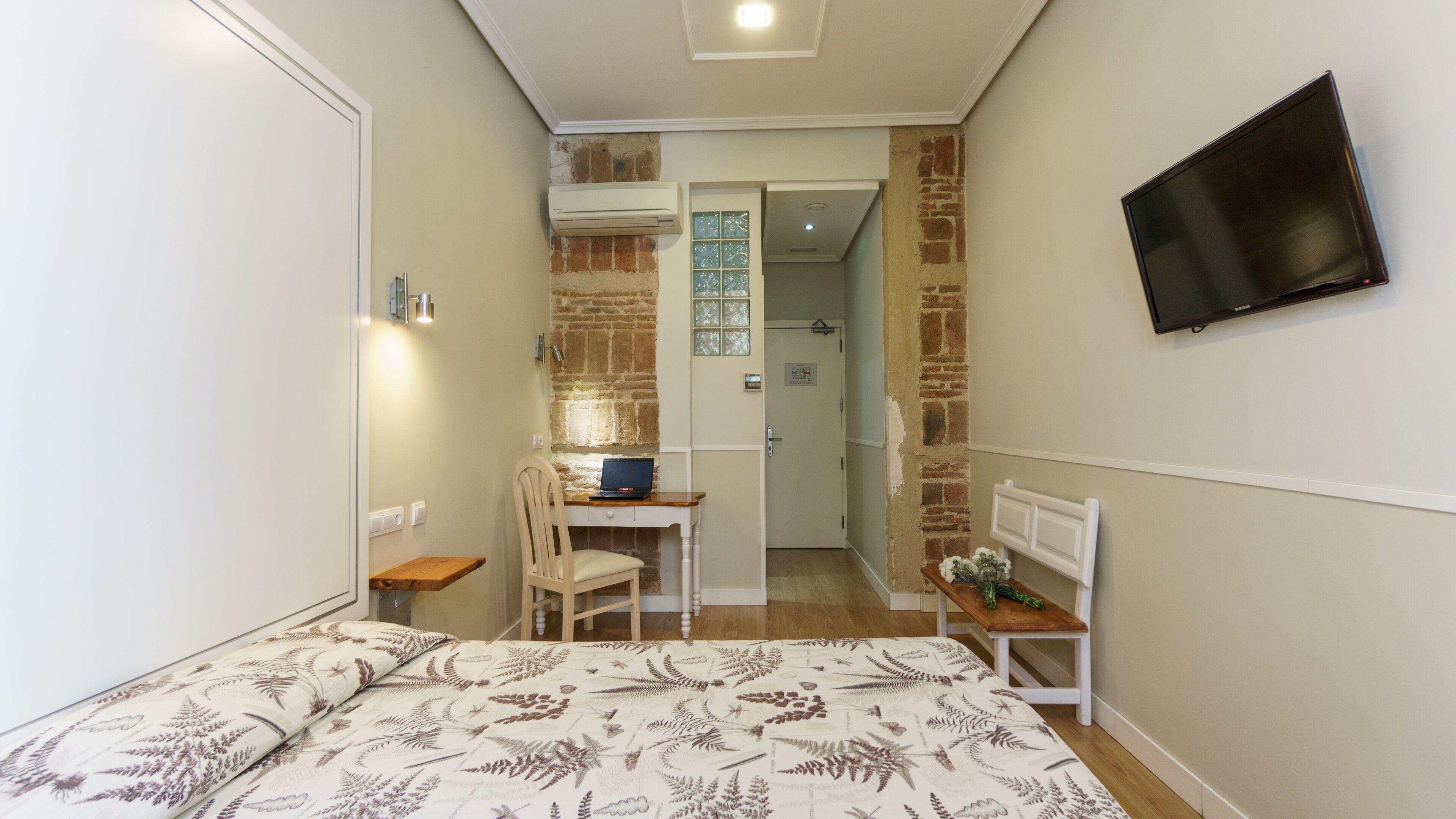 Una camera compatta con un letto, una scrivania e una televisione.