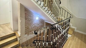 A modern staircase with a wooden finish and metal railings, leading to a lower level with a brick wall and a light fixture. - Hostal Madrid (Madrid)