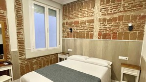 A bedroom with a brick wall, a window, a bed, a bedside table, and a nightstand. - Hostal Madrid (Madrid)