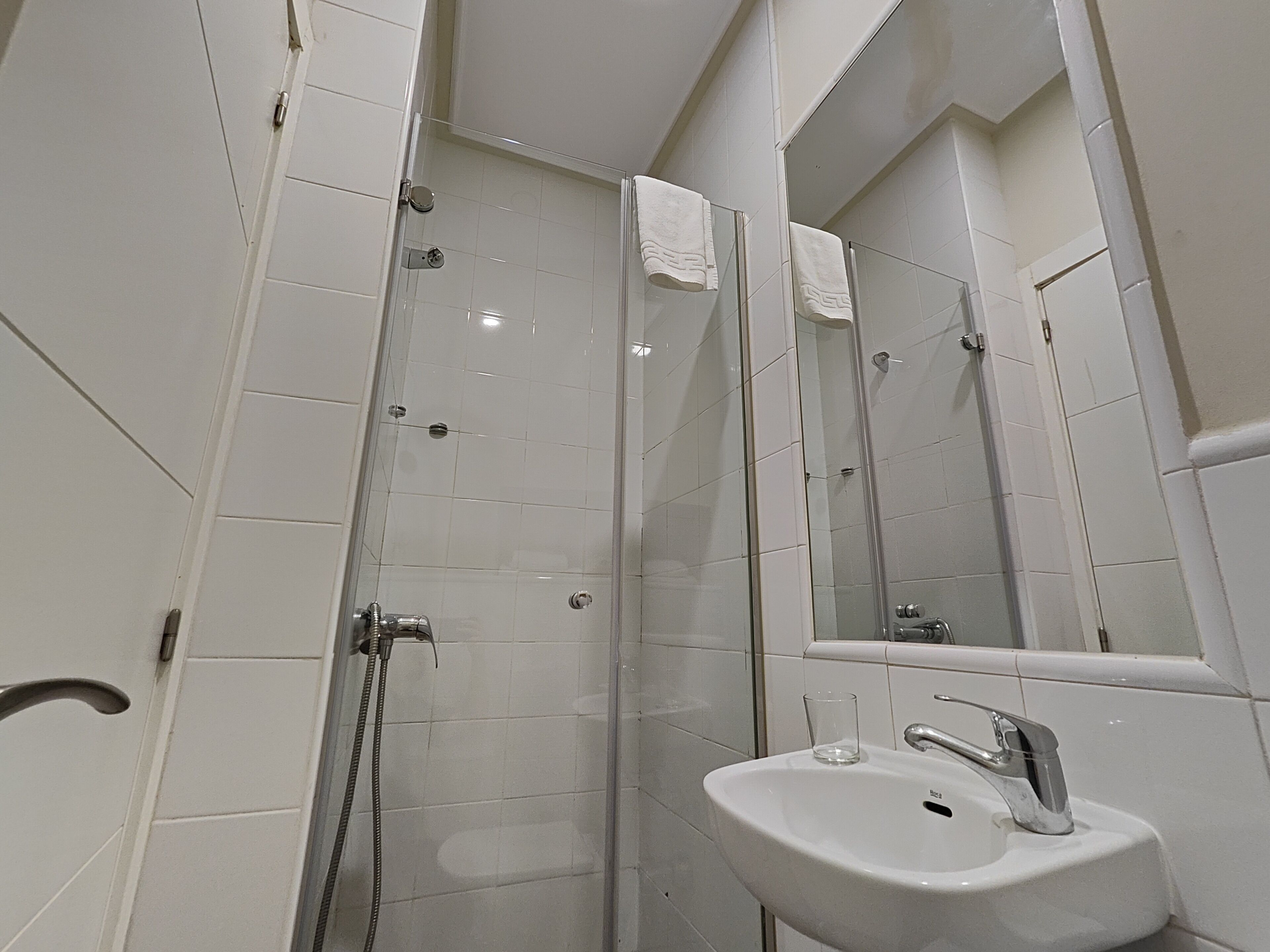 A modern bathroom with a glass-enclosed shower, a white sink with a glass, and a large mirror.