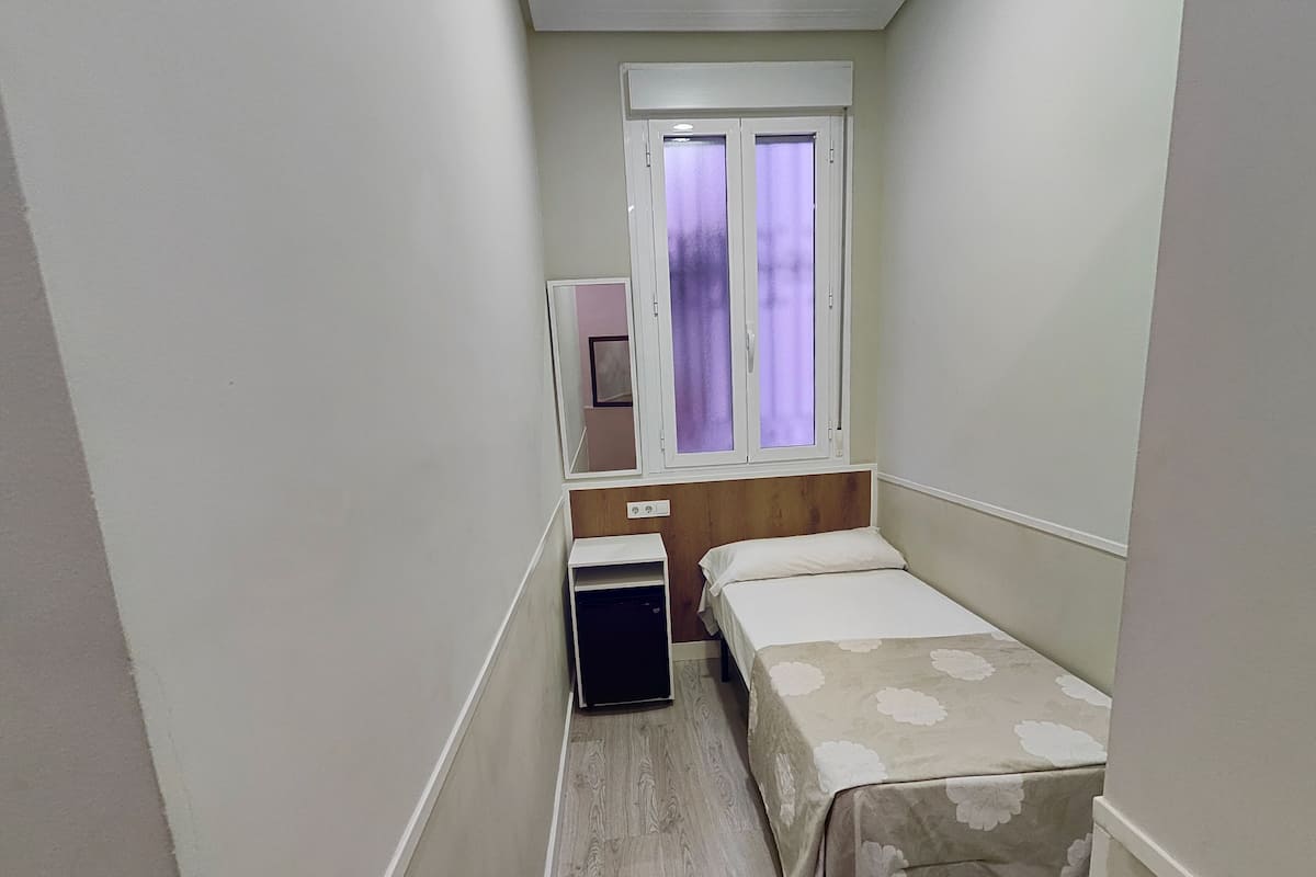 A narrow room with a bed, a small desk, and a window with frosted glass.