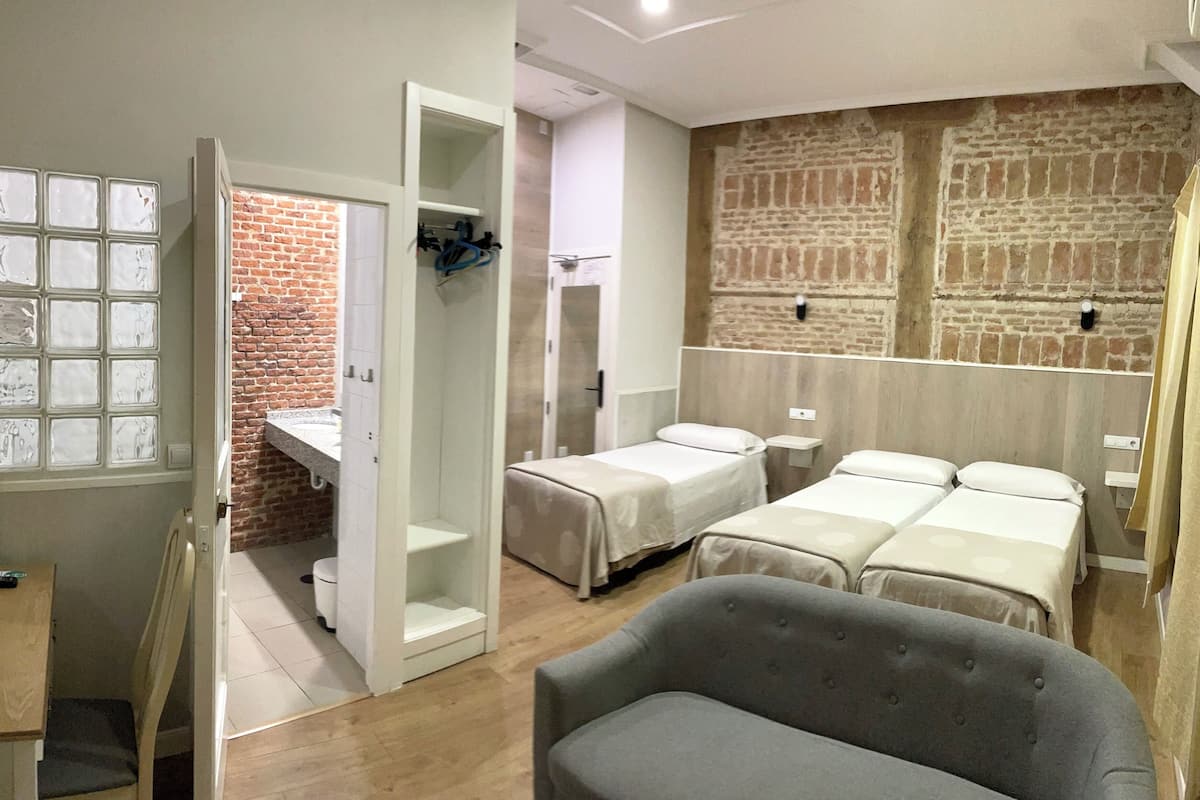 A hotel room with a brick wall, two beds, a desk, and a chair.