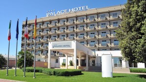 Un hôtel à plusieurs étages, doté de balcons, d’une entrée principale et de drapeaux.