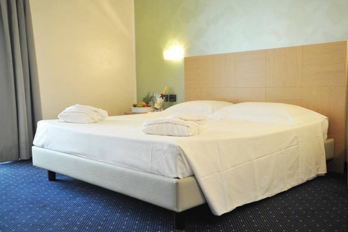 Hotellihuoneessa on valkoisilla lakanoiden päällä oleva parivuode.