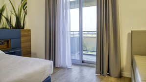 Une chambre d’hôtel avec un lit, un bureau, une plante en pot et un balcon avec des rideaux.
