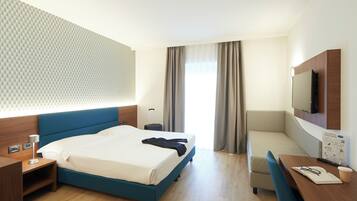 Habitación de hotel con cama, escritorio, silla, televisor y ventana con cortinas.