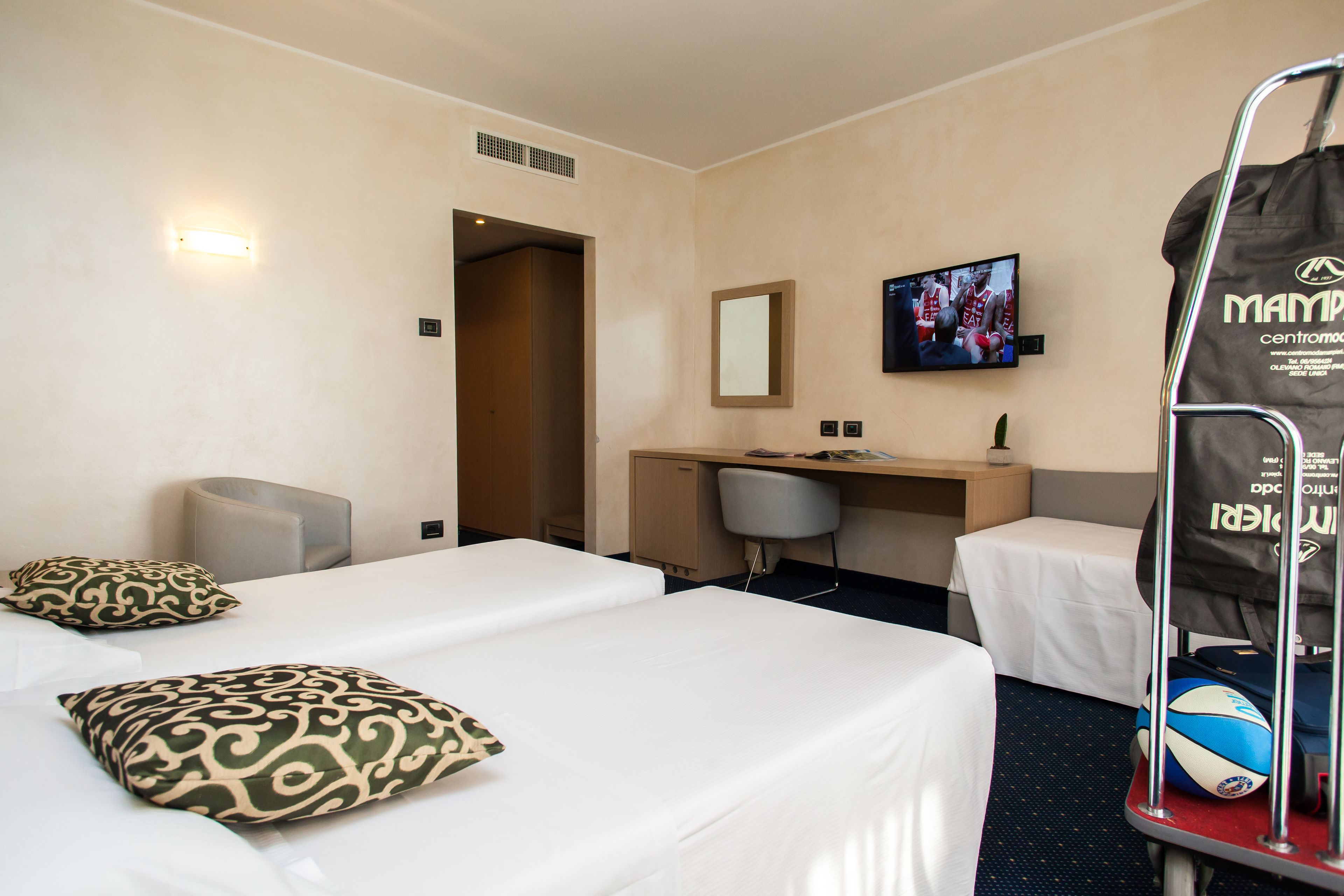 A hotel room with two beds, a desk, a chair, a TV, and a luggage cart.