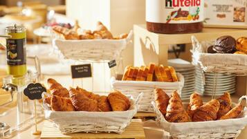 Un bufé de desayuno con cestas de cruasanes y otros pasteles, un tarro de Nutella y un dispensador de café.